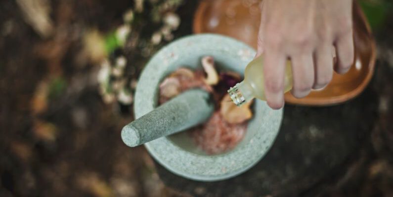 Organic Beauty - high angle photo of person pouring liquid from bottle inside mortar and pestle