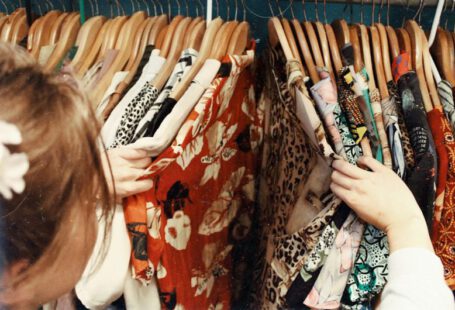 Online Vintage - person holding assorted clothes in wooden hanger