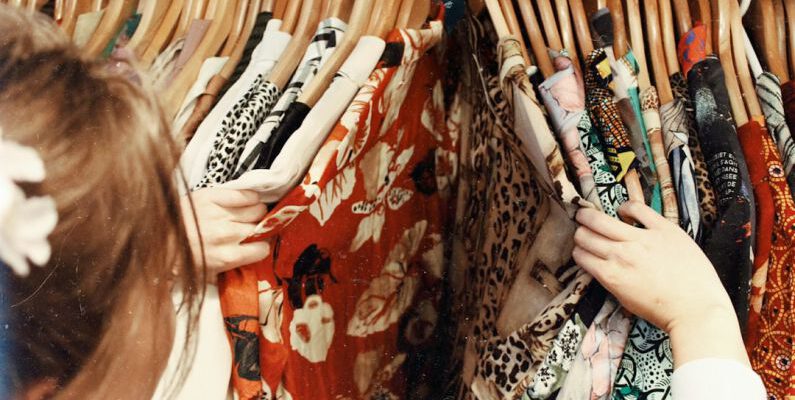 Online Vintage - person holding assorted clothes in wooden hanger