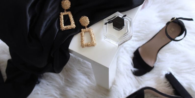 Sustainable Luxury - pair of gold-colored earrings on table and black ankle-strap pumps on area rug