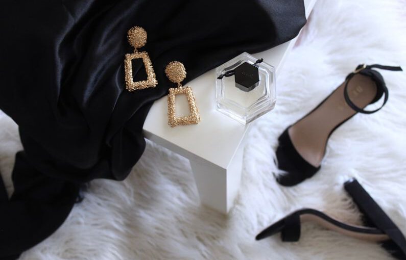 Sustainable Luxury - pair of gold-colored earrings on table and black ankle-strap pumps on area rug